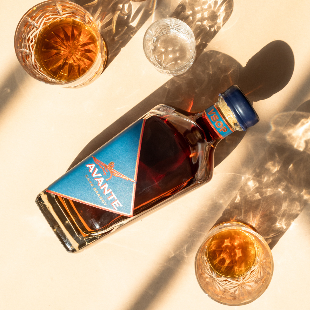 Avante Brandy VSOP Bottle lying face down on table with late afternoon sun rays reflecting off internal golden liquid.